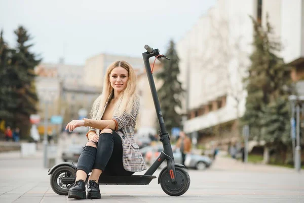 Beautiful young woman sitting on her electro scooter .