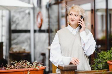 Çok güzel bir genç bayan, kafede otur ve kahve ya da çay iç, sokak manzaralı.