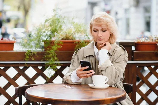 Fashionable woman talking by phone at outdoors cafe. Fashion and beauty. Technology and lifestyle concept. Stylish woman with perfect makeup and hairstyle. Seductive girl at coffee shop outside.