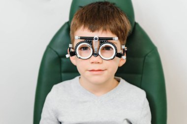 Genç bir çocuk klinikte gözlüklerle göz testi yaptırıyor.