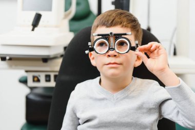 Genç bir çocuk klinikte gözlüklerle göz testi yaptırıyor.