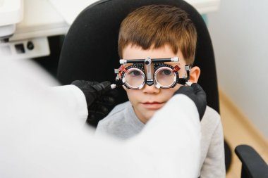 Gözlüklü neşeli çocuk göz doktorunu kontrol ediyor..