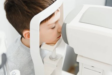 Bir çocukta vizyon düzeltmesi. Sabırlı çocuğun yakın plan yüzü. Modern bir klinikte göz muayenesi için süper modern ekipmanlar.