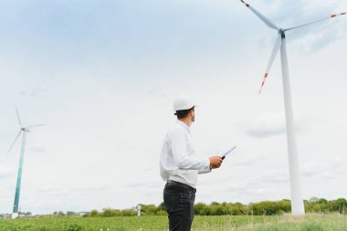 Rüzgar türbinleri elektrik üretiyor. Enerji koruma kavramı ve işçi kadrosu mühendisi tableti elinde tutuyor