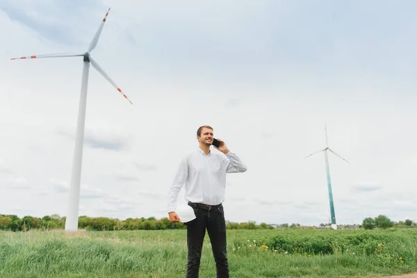 Windmill engineer talking on the phone on windmill and sky background. A man in a helmet supervises the operation of the electric windmills.