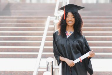 Neşeli Afro-Amerikan bayan mezun üniversite binasının önünde duruyor.