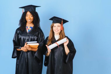 Mezuniyetlerini diplomalarla kutlayan iki genç kadın.