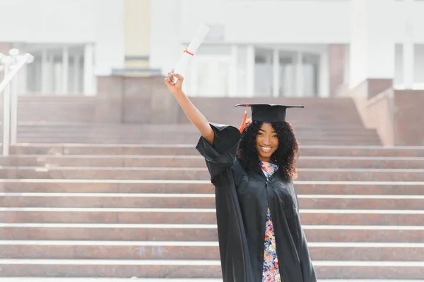 大学の建物の前に立つ陽気なアフリカ系アメリカ人女性の卒業生 — ストック写真
