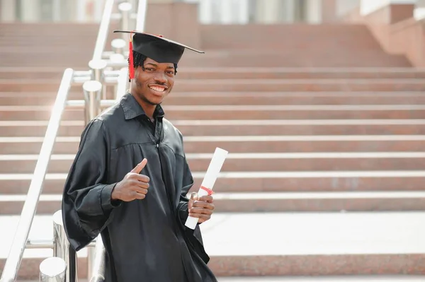 大学の建物の前に立つ若いアフリカの男性の卒業生は — ストック写真