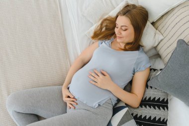 Gülümseyen hamile kadın yatak odasında dinleniyor.