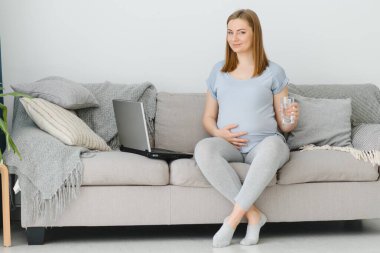 Bilgisayarın yanındaki koltukta oturan hamile serbest çalışanın yan görüntüsü.