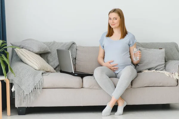 Wanita Hamil Dengan Segelas Air Duduk Sofa Muda Mengharapkan Pirang — Stok Foto