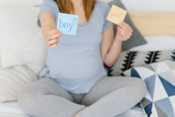 Pregnant woman with a sticky note and writing love boy or girl on sticky note and add on her belly,Pregnant Concept,Selective Focus