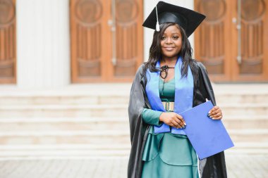 Mezuniyet elbisesi ve şapkası içinde diploması olan mutlu Hintli üniversite öğrencisi. Asya kökenli Hintli ve Afrikalı melez portresi.