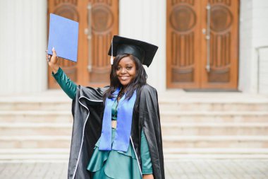 Mezuniyet elbisesi ve şapkası içinde diploması olan mutlu Hintli üniversite öğrencisi. Asya kökenli Hintli ve Afrikalı melez portresi.