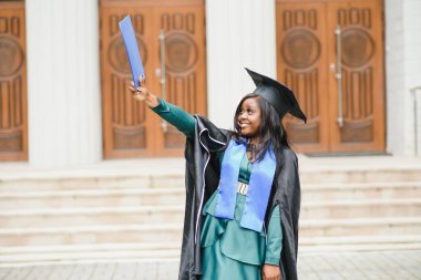 Mezuniyet elbisesi ve şapkası içinde diploması olan mutlu Hintli üniversite öğrencisi. Asya kökenli Hintli ve Afrikalı melez portresi.