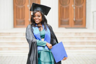 Mezuniyet elbisesi ve şapkası içinde diploması olan mutlu Hintli üniversite öğrencisi. Asya kökenli Hintli ve Afrikalı melez portresi.