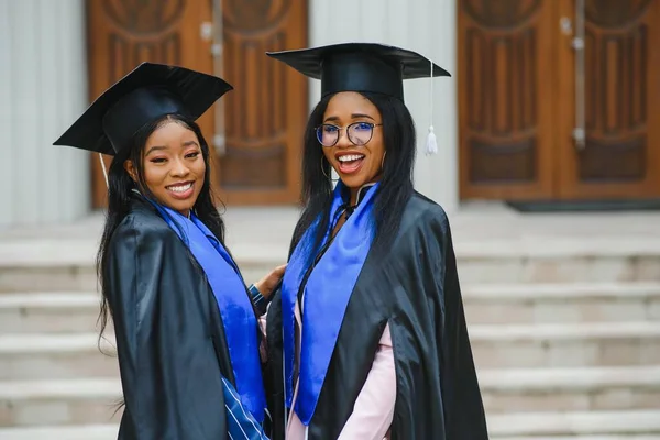 Duas Jovens Senhoras Trajes Formatura Posando Câmera Campus Universidade Segurando — Fotografia de Stock