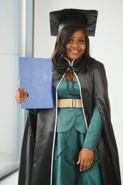 Mezuniyet elbisesi ve şapkası içinde diploması olan mutlu Hintli üniversite öğrencisi. Asya kökenli Hintli ve Afrikalı melez portresi.