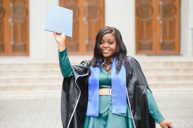 Mezuniyet elbisesi ve şapkası içinde diploması olan mutlu Hintli üniversite öğrencisi. Asya kökenli Hintli ve Afrikalı melez portresi.
