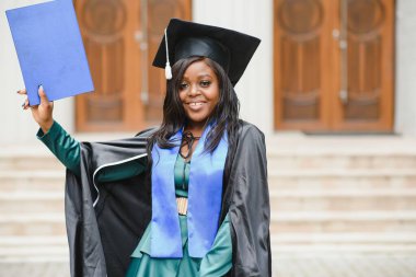 Mezuniyet elbisesi ve şapkası içinde diploması olan mutlu Hintli üniversite öğrencisi. Asya kökenli Hintli ve Afrikalı melez portresi.