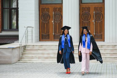 Mezuniyet gününde üniversite binasının önünde duran genç mezunlar.