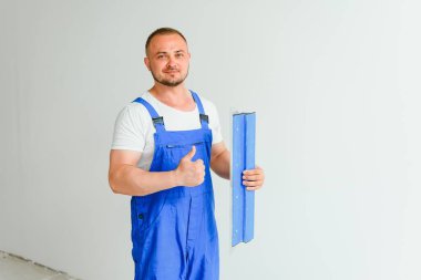 Tulum giymiş bir işçinin portresi ve arka plandaki duvarda macun bıçağını tutarken. Onarım ve inşaat konsepti