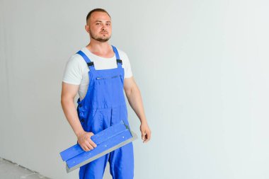 Tulumlu bir işçi duvarı çimentoyla kaplamak için bir mala kullanır.