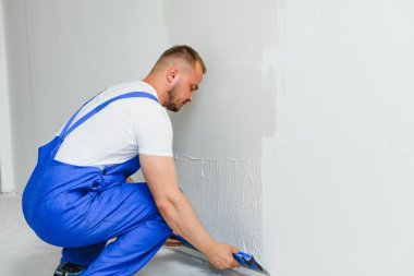 Tulumlu bir işçi duvarı çimentoyla kaplamak için bir mala kullanır.