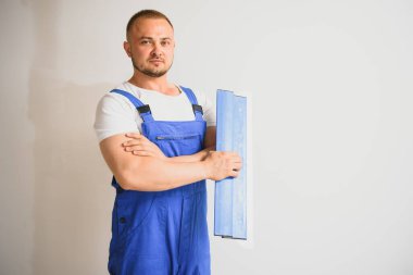 Tulum giymiş bir işçinin portresi ve arka plandaki duvarda macun bıçağını tutarken. Onarım ve inşaat konsepti