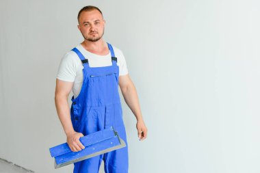 Bir adam duvarı spatula yla işler. Sıva lı iş yerinde.
