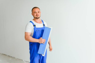 Tulumlu bir işçi duvarı çimentoyla kaplamak için bir mala kullanır.