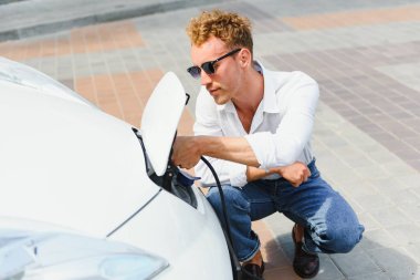 Şık bir adam şarj aletinin prizini yakın plan elektrikli arabanın prizine takar.