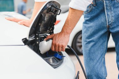 Şık bir adam şarj aletinin prizini yakın plan elektrikli arabanın prizine takar.