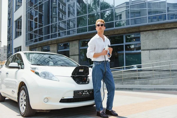 Adam Lüks Elektrikli Arabasını Modern Şehir Binalarının Önünde Şarj Ediyor — Stok fotoğraf