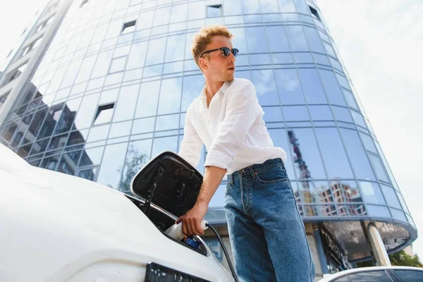 Genç Yakışıklı Adam Elektrik Şarj Istasyonunda Kablo Tutuyor Yeni Arabasının — Stok fotoğraf