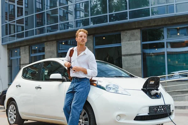 Cute young man near a modern electric car. The concept of ecological transport.