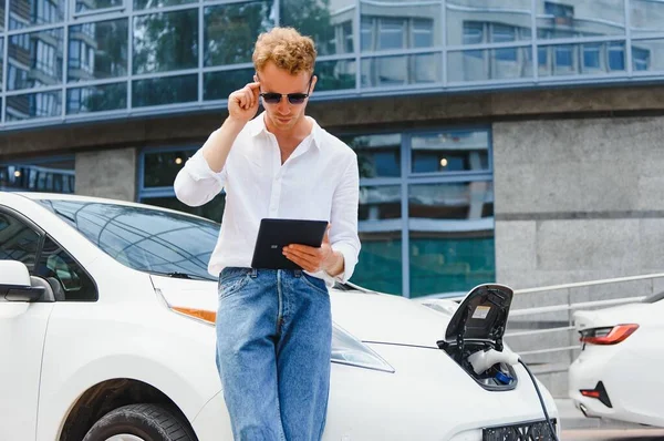 Geschäftsmann Steht Neben Dem Laden Von Elektroautos Und Nutzt Tablet — Stockfoto