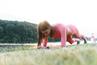 Genç beyaz kadın yazın nehir kenarındaki yoga minderinde aktif antrenman yapıyor. Sağlıklı yaşam tarzı kavramı