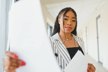 Afro-Amerikan iş kadını ayakta duruyor. Ofis salonu belgelerle dolu.