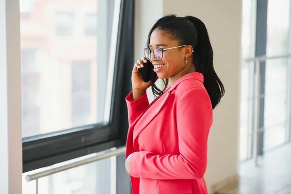 African-American businesswoman speaking by smartphone in office hall, copy space
