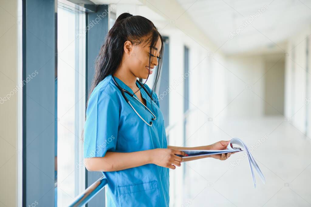 medicine, profession and healthcare concept - happy smiling african american female doctor with stethoscope over hospital background