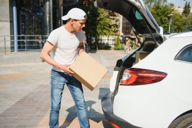 Gülümseyen teslimatçı arabasının önünde duruyor.