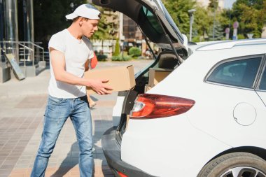 Gülümseyen teslimatçı arabasının önünde duruyor.