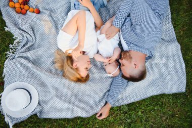 Genç bir aile yaz parkında bir battaniyenin üzerinde yatıyor.