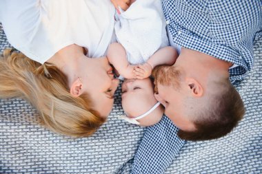 Anne, baba ve küçük oğlu yaz parkında battaniyenin üzerinde yatıyor. Yaz tatili kavramı. Anneler günü, babalar günü, bebekler günü. Aile doğada birlikte vakit geçiriyor. Aile görünüşü