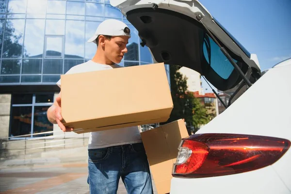 Deliveryman holds parcels at the car, delivering