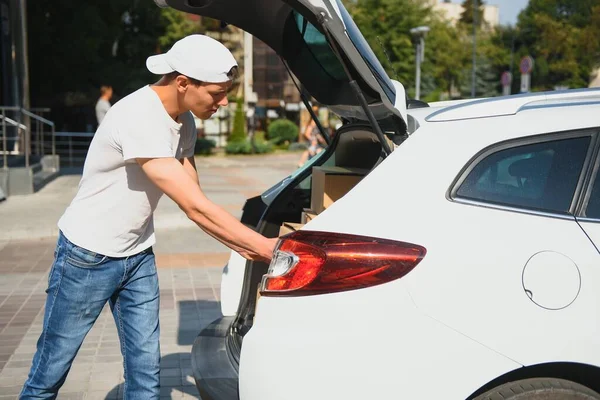 Deliveryman holds parcels at the car, delivering