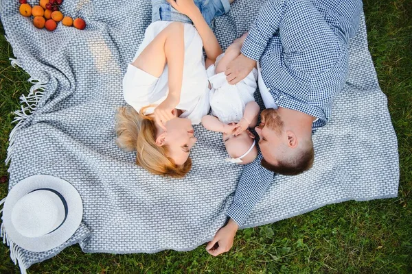 Genç bir aile yaz parkında bir battaniyenin üzerinde yatıyor.