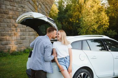 Bagajları açık arabanın bagajında duran genç çift kameraya bakıyor.